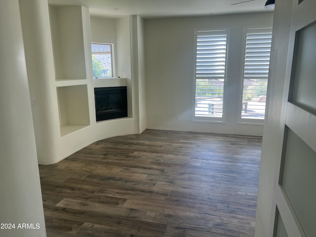 spare room featuring built in shelves, dark hardwood / wood-style flooring, and a healthy amount of sunlight