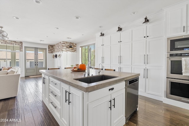 kitchen with dark wood-type flooring, white cabinets, appliances with stainless steel finishes, and a kitchen island with sink