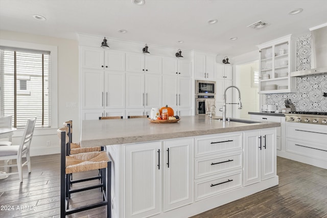 kitchen with white cabinets, appliances with stainless steel finishes, a kitchen island with sink, dark wood-type flooring, and sink