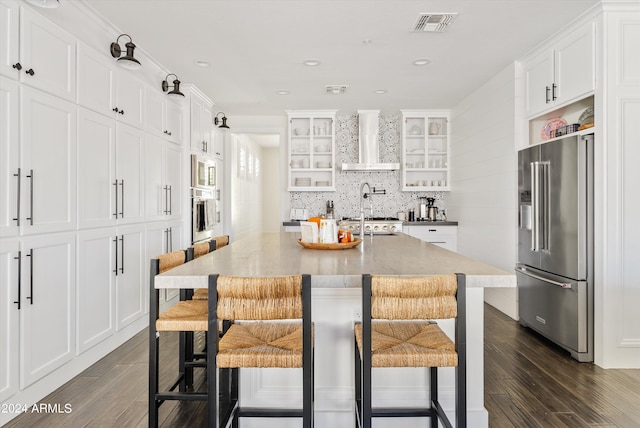 kitchen featuring a breakfast bar, wall chimney exhaust hood, stainless steel appliances, and a center island with sink