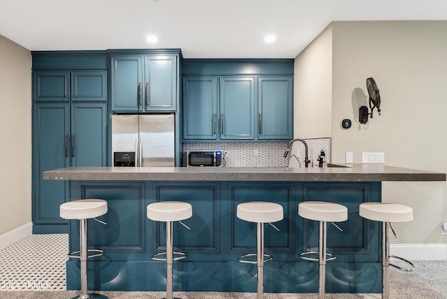 kitchen with a kitchen bar, backsplash, kitchen peninsula, blue cabinets, and stainless steel fridge