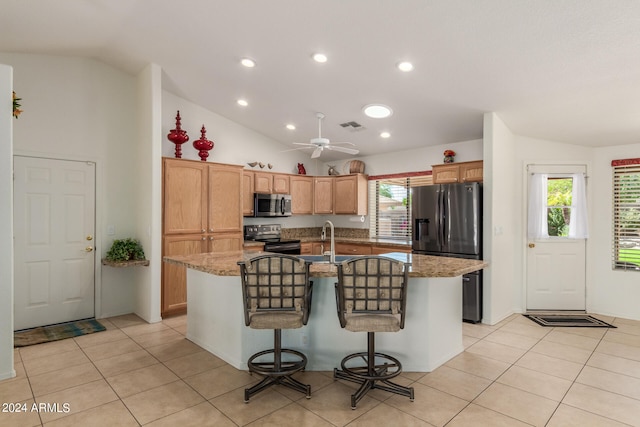 kitchen featuring lofted ceiling, appliances with stainless steel finishes, light stone counters, and a kitchen island with sink