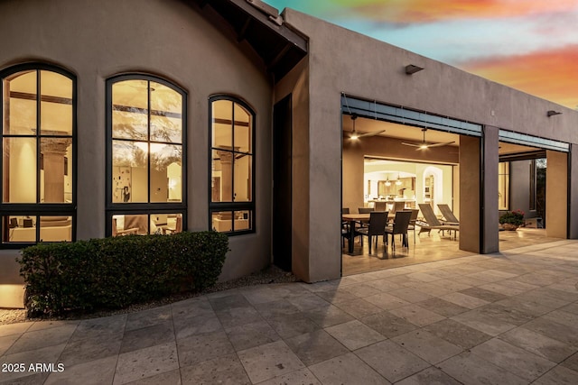 rear view of property with ceiling fan, a patio, outdoor dining space, and stucco siding