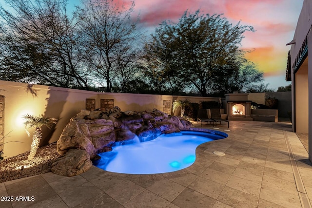 view of pool with a warm lit fireplace, a fenced in pool, and a patio