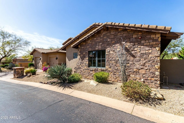 view of front of property featuring a garage, stone siding, a tiled roof, and stucco siding