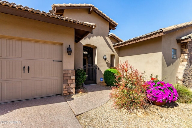 view of exterior entry with a garage, a gate, driveway, and stucco siding