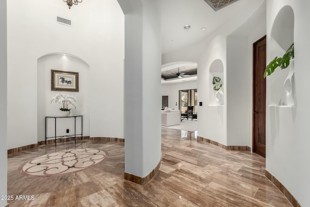 corridor with marble finish floor, baseboards, visible vents, and arched walkways