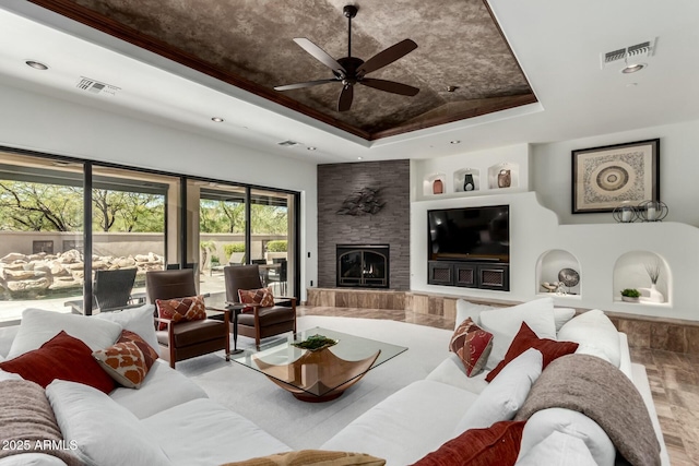 living room with a tray ceiling, a large fireplace, visible vents, and ceiling fan