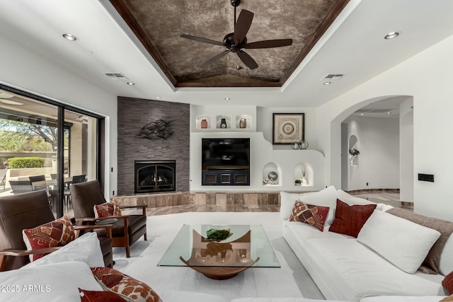 living room featuring arched walkways, recessed lighting, a raised ceiling, visible vents, and a large fireplace