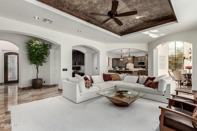 living area featuring recessed lighting, a raised ceiling, visible vents, baseboards, and ceiling fan with notable chandelier