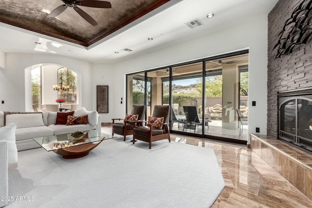 living area featuring arched walkways, recessed lighting, a fireplace, visible vents, and a raised ceiling