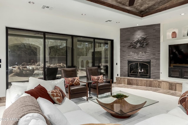 living area with a large fireplace, visible vents, a tray ceiling, and recessed lighting