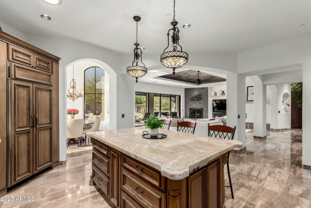 kitchen featuring arched walkways, marble finish floor, a large fireplace, a kitchen island, and a kitchen breakfast bar