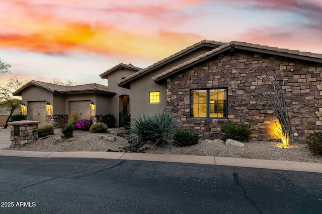 view of front of house featuring a garage, stone siding, a tile roof, and stucco siding