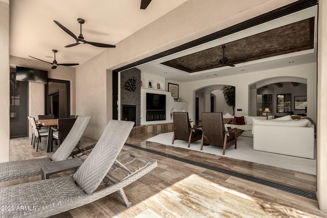 interior space featuring arched walkways, a fireplace, ceiling fan, and a tray ceiling