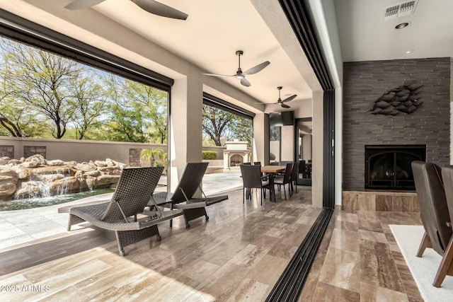 view of patio featuring visible vents, exterior fireplace, ceiling fan, and outdoor dining space