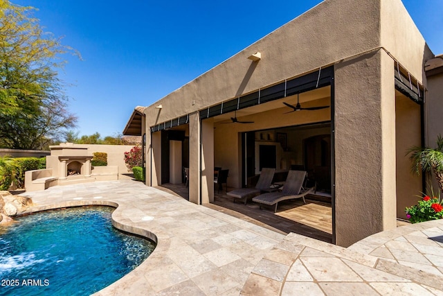 back of property with a patio area, exterior fireplace, a ceiling fan, and stucco siding