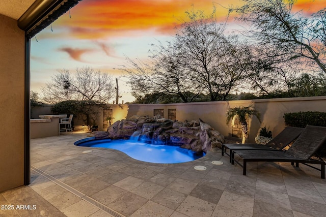 pool at dusk featuring outdoor dry bar, a patio, a fenced backyard, and a fenced in pool