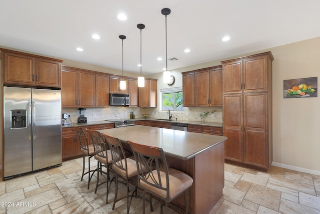 kitchen featuring sink, decorative light fixtures, appliances with stainless steel finishes, a kitchen breakfast bar, and a center island