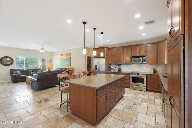 kitchen with decorative light fixtures, backsplash, stainless steel appliances, a center island, and a breakfast bar area