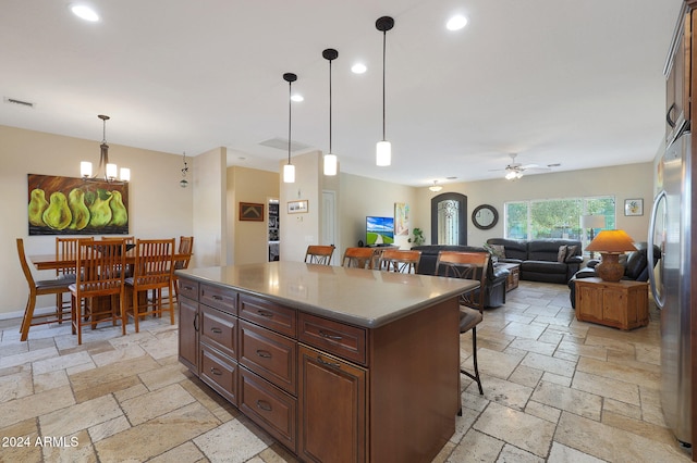 kitchen featuring ceiling fan with notable chandelier, decorative light fixtures, a center island, and a breakfast bar