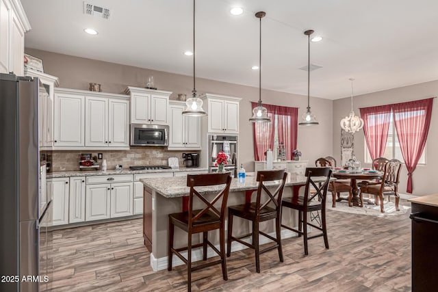 kitchen with visible vents, white cabinets, an island with sink, stainless steel appliances, and pendant lighting