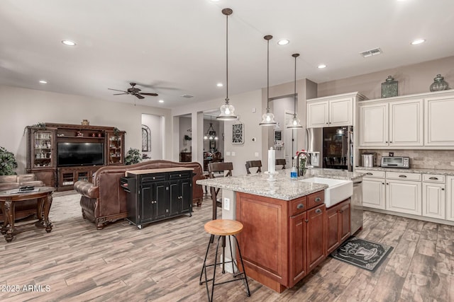 kitchen with a breakfast bar area, hanging light fixtures, open floor plan, a kitchen island with sink, and white cabinetry