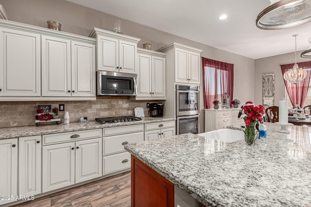 kitchen with a chandelier, stainless steel appliances, white cabinets, decorative backsplash, and pendant lighting