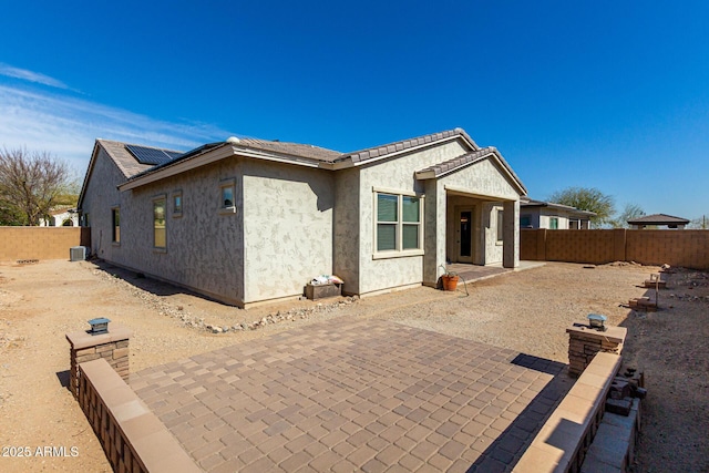 view of front of house with a patio, solar panels, central air condition unit, stucco siding, and a fenced backyard