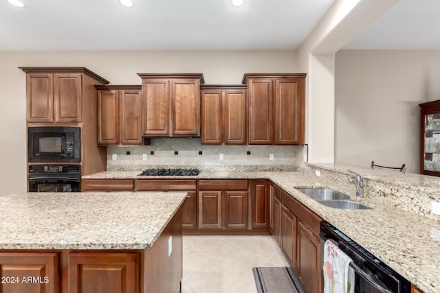 kitchen with light stone counters, kitchen peninsula, black appliances, backsplash, and sink