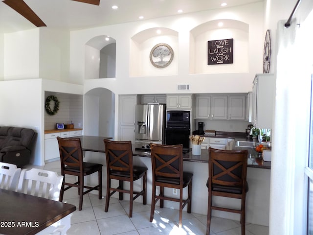 kitchen featuring black microwave, gray cabinetry, a kitchen breakfast bar, stainless steel fridge with ice dispenser, and dark countertops