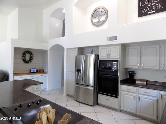 kitchen featuring light tile patterned floors, dark countertops, visible vents, a towering ceiling, and black appliances