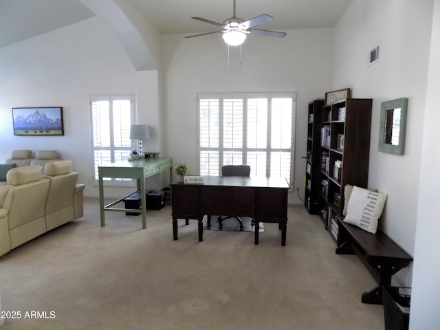 office space with a ceiling fan, a towering ceiling, visible vents, and light colored carpet