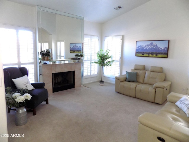 living room with visible vents, vaulted ceiling, a tiled fireplace, and light colored carpet