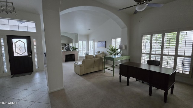 interior space featuring arched walkways, light colored carpet, a high ceiling, light tile patterned flooring, and a tile fireplace