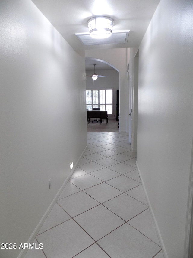 hallway featuring light tile patterned floors, baseboards, and arched walkways