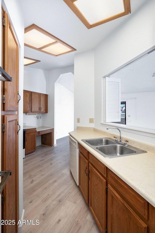 kitchen with white dishwasher, built in desk, sink, and light wood-type flooring