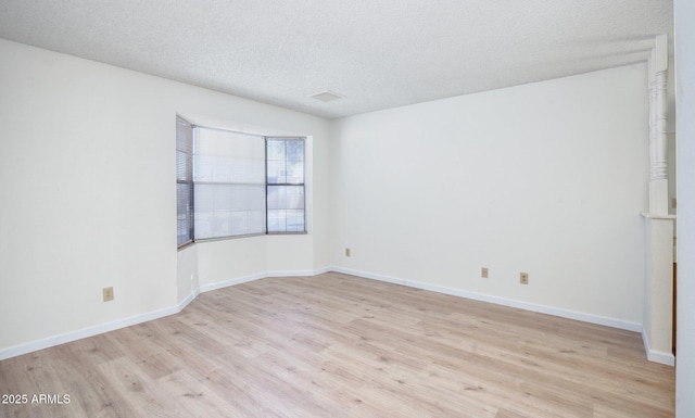 empty room with light wood-type flooring and a textured ceiling