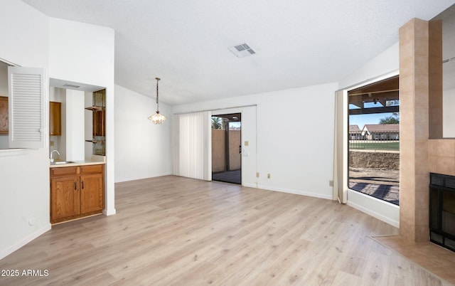 unfurnished living room with sink, a chandelier, a textured ceiling, a fireplace, and light hardwood / wood-style floors