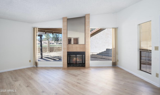 unfurnished living room featuring lofted ceiling, light hardwood / wood-style flooring, a tile fireplace, and a textured ceiling