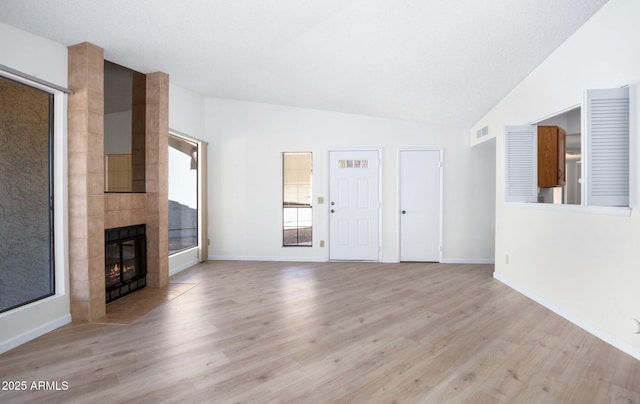 unfurnished living room with a tiled fireplace, vaulted ceiling, and light wood-type flooring