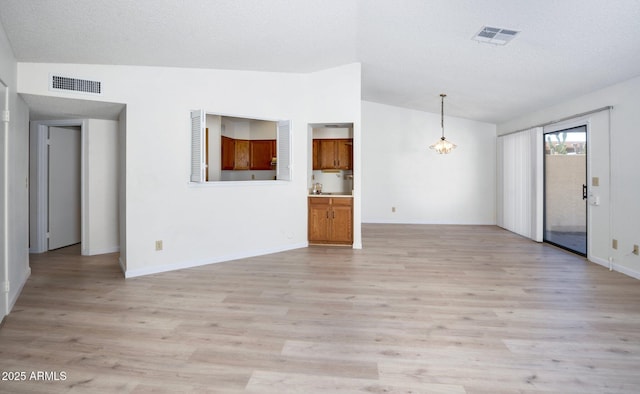 unfurnished living room with a notable chandelier, light hardwood / wood-style flooring, a textured ceiling, and vaulted ceiling