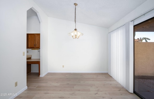 unfurnished dining area featuring an inviting chandelier, vaulted ceiling, and light wood-type flooring