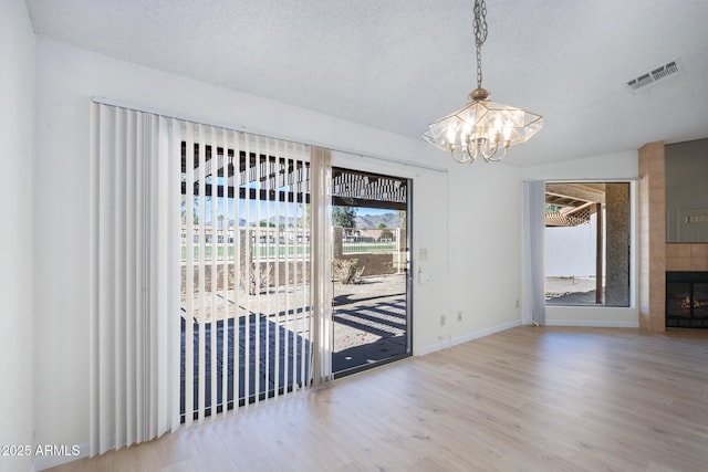 unfurnished dining area featuring a notable chandelier, a textured ceiling, a fireplace, and wood-type flooring