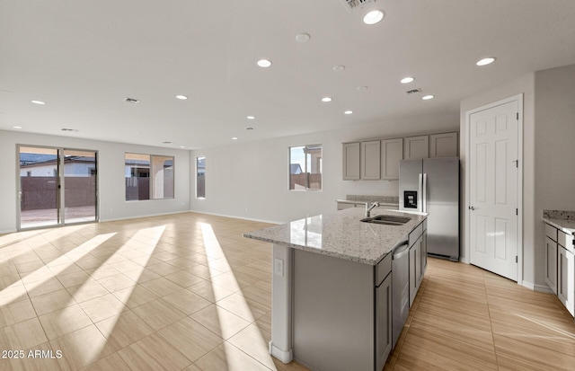 kitchen with gray cabinets, light tile patterned flooring, sink, stainless steel appliances, and a center island with sink