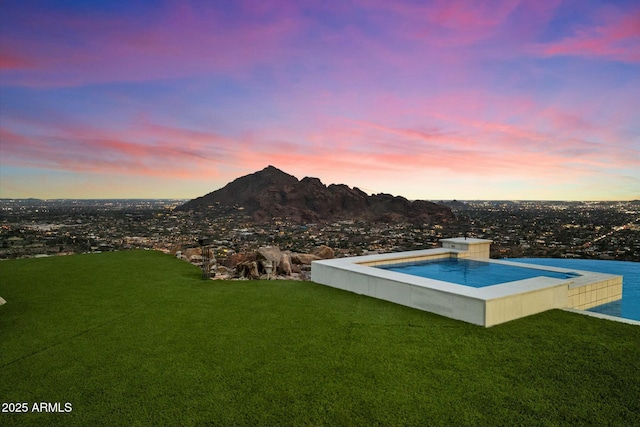 pool at dusk with a mountain view and a yard