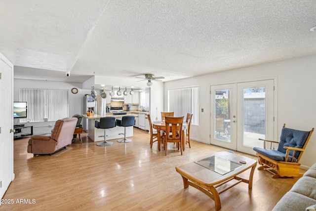 living room featuring ceiling fan, french doors, a textured ceiling, and light wood-type flooring