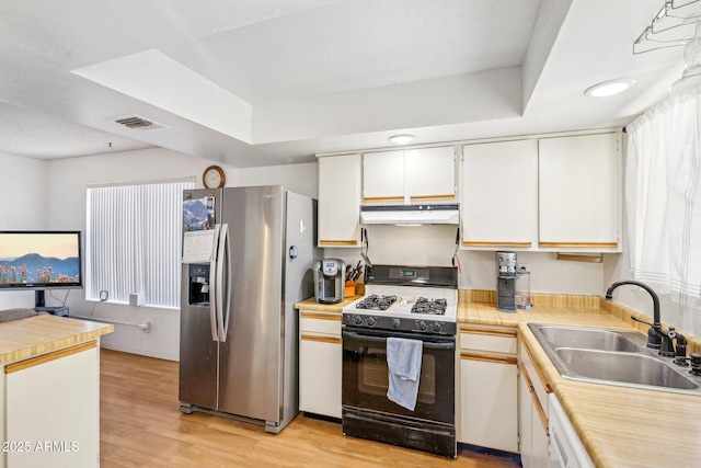 kitchen featuring stainless steel refrigerator with ice dispenser, sink, gas range, a raised ceiling, and white cabinets