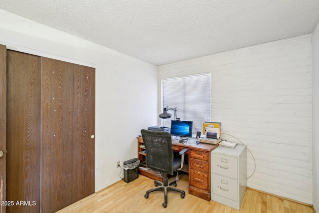 home office with brick wall, light hardwood / wood-style flooring, and a textured ceiling