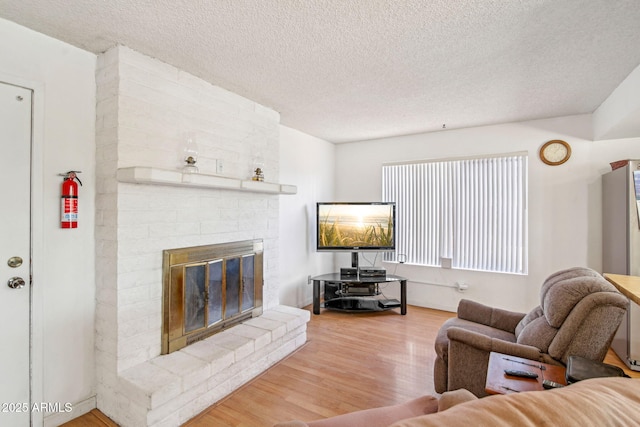 living room with hardwood / wood-style flooring, a brick fireplace, and a textured ceiling